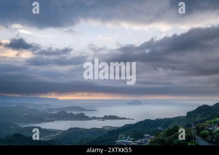Von der Spitze des Berges aus entfaltet sich eine nebelbehüllte Landschaft, die ein malerisches Küstendorf inmitten sanfter Hügel zeigt. Jiufen, Taiwan. Stockfoto