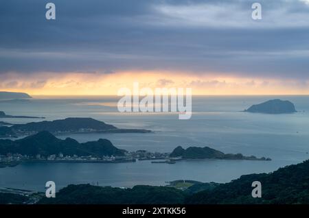 Von der Spitze des Berges aus entfaltet sich eine nebelbehüllte Landschaft, die ein malerisches Küstendorf inmitten sanfter Hügel zeigt. Jiufen, Taiwan. Stockfoto