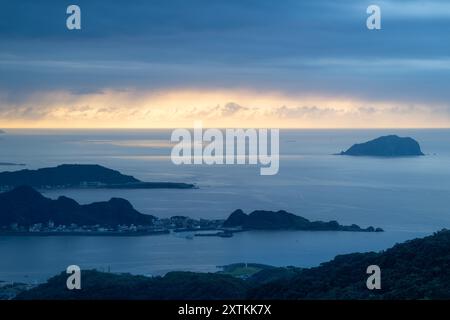 Von der Spitze des Berges aus entfaltet sich eine nebelbehüllte Landschaft, die ein malerisches Küstendorf inmitten sanfter Hügel zeigt. Jiufen, Taiwan. Stockfoto