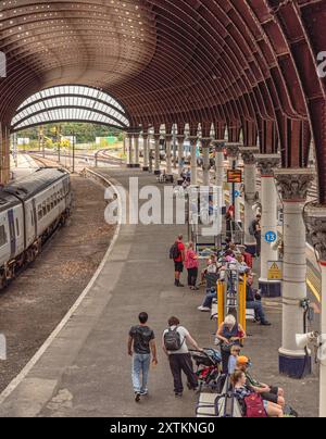 Blick nach unten auf den Bahnsteig des Bahnhofs mit Fahrgästen, die auf Züge warten. Ein Zug befindet sich auf einer Seite und über dem Hotel befindet sich eine historische Eisenkugel aus dem 19. Jahrhundert Stockfoto