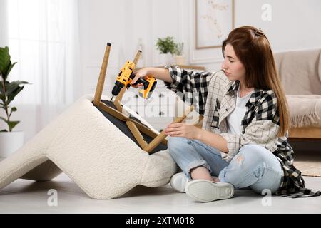 Frau mit elektrischem Schraubenzieher, der den Sessel zu Hause zusammenbaut Stockfoto