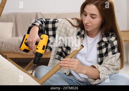 Frau mit elektrischem Schraubenzieher, der den Sessel zu Hause zusammenbaut Stockfoto