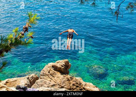 Sonnenbaden und Schwimmen auf den Felsen rund um Cavtat in Südkroatien - ein Mann taucht von einem Felsen in das krustfreie Wasser ein. Stockfoto