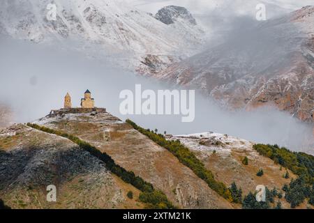 Blick auf die Gergeti Trinity Kirche auf einem Hügel direkt vor dem Berg Kasbek (versteckt in den Wolken) in Kazbegi, Georgia Stockfoto