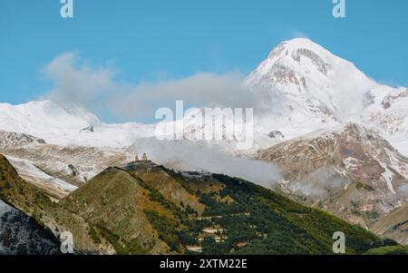 Die Gergeti Trinity Church thront auf einem Hügel mit dem schneebedeckten Berg Kasbek im Hintergrund, unter einem leuchtend blauen Himmel in Georgien. Stockfoto