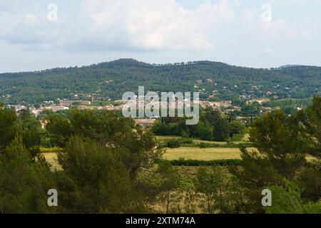 Ein Blick auf ein üppiges, grünes französisches Dorf, umgeben von Bäumen, mit einer fernen Bergkette im Hintergrund, unter einem teilweise bewölkten Himmel. Stockfoto