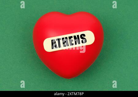 Ein leuchtend rotes Herz zeigt stolz den Namen Athen, der die Zuneigung zu dieser historischen Hauptstadt vor einem einfachen grünen Hintergrund darstellt. Stockfoto