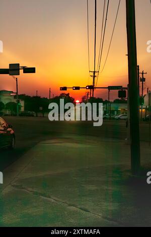 Die Sonne steht tief am Horizont und strahlt ein warmes, goldenes Licht auf der anderen Straßenseite aus, gesäumt von Gebäuden und Autos. Stockfoto