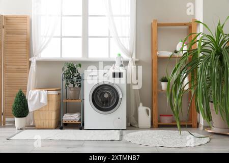 Waschmaschine, Wäschekorb und Klappschirm neben dem Fenster im Zimmer Stockfoto