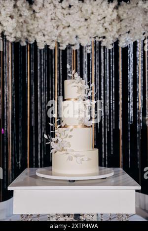 Hochzeitseinrichtung mit dreistufigem weißem Kuchen mit Blumenakzenten. Hochzeitsinspiriert, luxuriöse Veranstaltungen Stockfoto
