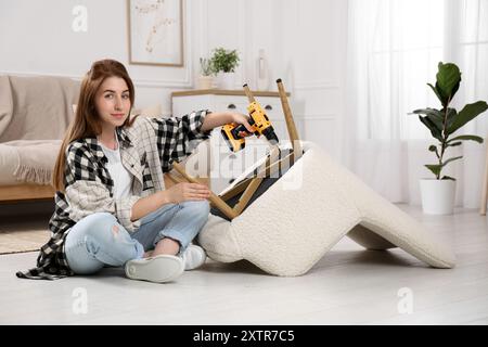 Frau mit elektrischem Schraubenzieher, der den Sessel zu Hause zusammenbaut Stockfoto