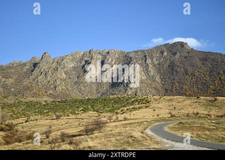 Majestätischer felsiger Berg unter klarem blauem Himmel, eine gewundene Straße durchquert das zerklüftete Gelände und unterstreicht die ruhige Schönheit der Natur. Stockfoto