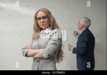 Ein älterer Mann schreibt auf ein Whiteboard und eine junge Frau steht nachdenklich. Stockfoto
