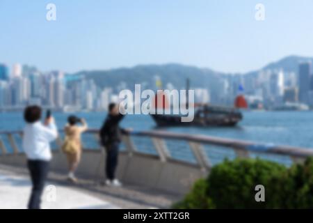 Verschwommener Blick auf den Victoria Harbour in Hongkong, China, mit Touristen, die Fotos von einem traditionellen chinesischen Dschunkenboot machen. Stockfoto