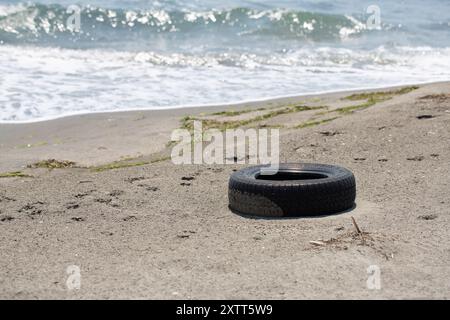 Der alte Reifen liegt an einem Sandstrand und verschmutzt die natürliche Umwelt Stockfoto