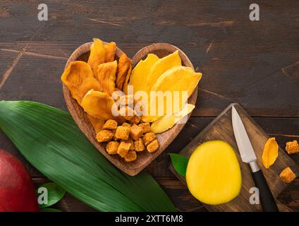 Hölzerne Platte in Herzform mit getrockneten Mangoblättern und Kugeln mit frischem Obst. Stockfoto