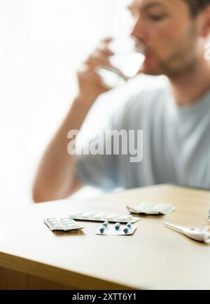 Der Mann nimmt Medikamente, der Patient trinkt Pillen, liest medizinische Rezepte, Blasen mit Pillen auf dem Tisch Stockfoto