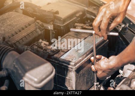 Ein Kfz-Techniker zerlegt eine alte Batterie in einem Auto mit einem Schraubenschlüssel. Batteriewechsel des Fahrzeugs. Der Motor ist im Hintergrund sichtbar, und Stockfoto