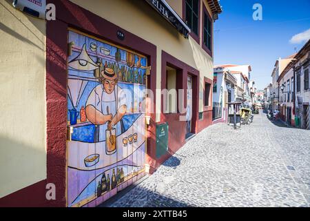 Ein Wandbild einer Person, die ein traditionelles Poncha-Getränk herstellt, abgebildet in der Santa Maria Street in Funchal, Madeira am 9. August 2024 als Teil der Kunst des O Stockfoto