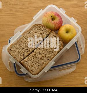 Gesundes Lunchpaket mit hausgemachten braunen Vollkornbrotsandwiches und Mini-Äpfeln in einer transparenten „Lock and Lock“-Lunchbox aus Kunststoff Stockfoto