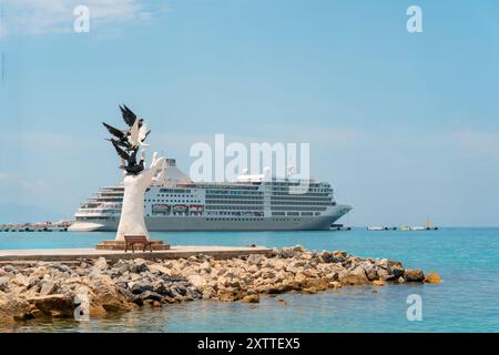 Aydin Kusadasi, Türkei - 4. Juli 2024: Hand des Friedens Skulptur und Kreuzfahrtschiff dahinter in Kusadasi Aydin Stockfoto