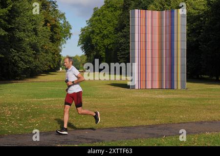 Ein Jogger passiert Gerhard Richters Kunstinstallation Strip-Tower im Londoner Hyde Park. Großbritannien wird dieses Wochenende Höchsttemperaturen von 25 °C erleben, da sich die Temperaturen nach einer Woche, an der bisher der heißeste Tag des Jahres war, stabilisieren. Bilddatum: Freitag, 16. August 2024. Stockfoto