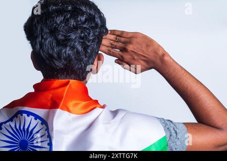 Eine junge Person, die mit einer indischen Flagge auf weißem Hintergrund über der Schulter grüßt. Patriotismus und Nationalstolz. Stockfoto