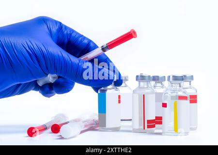 Hand in blauem Handschuh, der Spritze und Durchstechflaschen mit Medikament auf weißem Hintergrund hält Stockfoto