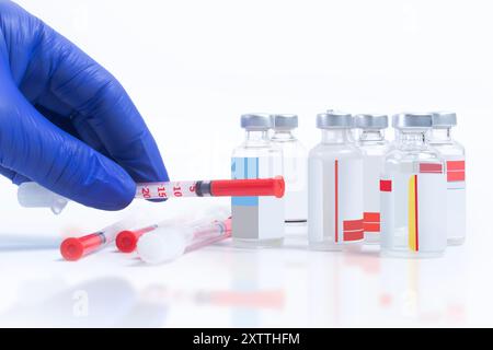 Blauer Arzt mit Handschuhen, der Spritze hält und einen Stapel Spritzen, der mit Durchstechflaschen auf weißem Hintergrund liegt Stockfoto