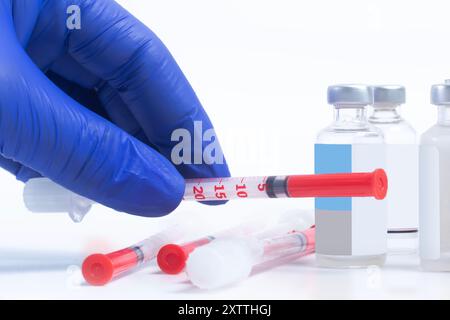 Blauer Arzt mit Handschuhen, der Spritze hält und einen Stapel Spritzen, der mit Durchstechflaschen auf weißem Hintergrund liegt Stockfoto