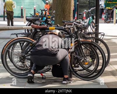 Radfahrerin, die das Fahrrad an der Fahrradschiene in Zentral-London einsperrt Stockfoto