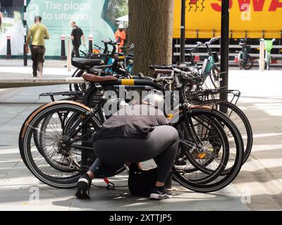 Radfahrerin, die das Fahrrad an der Fahrradschiene in Zentral-London einsperrt Stockfoto