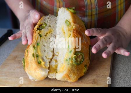 Hände halten einen geschnittenen Brotlaib mit jalapeño-Belag und zeigen den Stockfoto