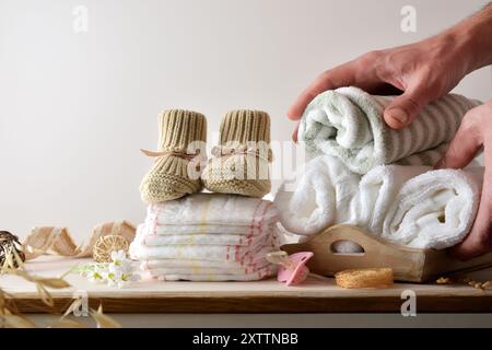 Hände bereiten Tücher und Windeln für die Babyhygiene auf Holzmöbeln mit Stiefeln, Schnuller und Dekoration vor. Vorderansicht. Stockfoto