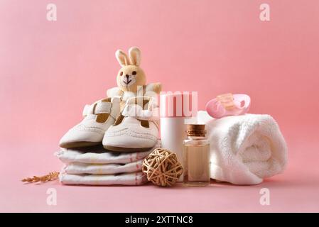 Pflegeprodukte für kleines Mädchen mit Talkum und Lotion auf rosa Hintergrund mit Windeln, Schnuller, Schuhen, Handtuch und Dekoration. Vorderansicht. Stockfoto