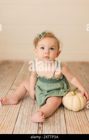 Blauäugiges Mädchen, das auf Holzboden sitzt und weißen Kürbis hält Stockfoto