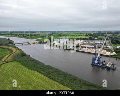 Elsfleth, Deutschland. August 2024. Der Schwimmkran Athlet bringt den 24 Meter langen und 58 Tonnen schweren Brückenabschnitt als Ersatz für die wenige Wochen zuvor von einem Tankfahrzeug gerammte Eisenbahnbrücke. Diese Brücke war auch eine provisorische Brücke, da bereits im Februar ein Lastkahn auf die reguläre Eisenbahnbrücke traf. Die Brücke und die Freileitungen wurden so stark beschädigt, dass der Zugverkehr eingestellt werden musste. (Foto mit einer Drohne) Lars Penning/dpa/Alamy Live News Stockfoto