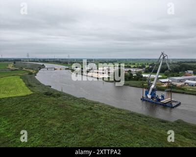 Elsfleth, Deutschland. August 2024. Der Schwimmkran Athlet bringt den 24 Meter langen und 58 Tonnen schweren Brückenabschnitt als Ersatz für die wenige Wochen zuvor von einem Tankfahrzeug gerammte Eisenbahnbrücke. Diese Brücke war auch eine provisorische Brücke, da bereits im Februar ein Lastkahn auf die reguläre Eisenbahnbrücke traf. Die Brücke und die Freileitungen wurden so stark beschädigt, dass der Zugverkehr eingestellt werden musste. (Foto mit einer Drohne) Lars Penning/dpa/Alamy Live News Stockfoto