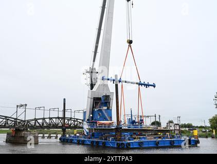 Elsfleth, Deutschland. August 2024. Der Schwimmkran Athlet bringt den 24 Meter langen und 58 Tonnen schweren Brückenabschnitt als Ersatz für die wenige Wochen zuvor von einem Tankfahrzeug gerammte Eisenbahnbrücke. Diese Brücke war auch eine provisorische Brücke, da bereits im Februar ein Lastkahn auf die reguläre Eisenbahnbrücke traf. Die Brücke und die Freileitungen wurden so stark beschädigt, dass der Zugverkehr eingestellt werden musste. (Foto mit einer Drohne) Lars Penning/dpa/Alamy Live News Stockfoto