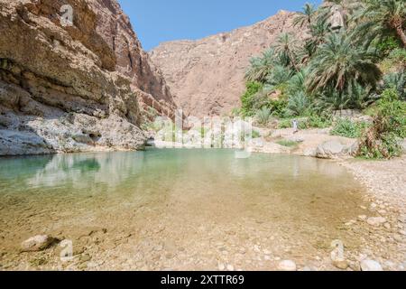Ein Mann, der durch die Schlucht von Wadi Ash Shab's im Sultanat Oman geht, einem beliebten Reiseziel aus dem Nahen Osten, mit Kopierraum im Fluss Stockfoto