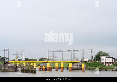 Elsfleth, Deutschland. August 2024. Die Arbeiter stellen sicher, dass die Brücke perfekt sitzt, damit die neue provisorische Brücke beim Anheben an ihrem Platz ist. Der „Athlet“-Schwimmkran bringt den 24 Meter langen und 58 Tonnen schweren Brückenabschnitt als Ersatz für die Eisenbahnbrücke, die einige Wochen zuvor von einem Tankfahrzeug gerammt wurde. Diese Brücke war auch eine provisorische Brücke, da bereits im Februar ein Lastkahn auf die reguläre Eisenbahnbrücke traf. Die Brücke und die Freileitungen wurden so stark beschädigt, dass der Zugverkehr eingestellt werden musste. Quelle: Lars Penning/dpa/Alamy Live News Stockfoto