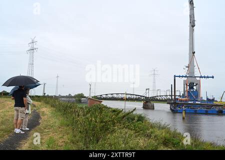 Elsfleth, Deutschland. August 2024. Die Familie Wallinger wirft trotz Regen einen Blick auf die Brückenbaustelle. Der „Athlet“-Schwimmkran bringt den 24 Meter langen, 58 Tonnen schweren Brückenabschnitt als Ersatz für die Eisenbahnbrücke, die einige Wochen zuvor von einem Tankfahrzeug gerammt wurde. Diese Brücke war auch eine provisorische Brücke, da bereits im Februar ein Lastkahn auf die reguläre Eisenbahnbrücke traf. Die Brücke und die Freileitungen wurden so stark beschädigt, dass der Zugverkehr eingestellt werden musste. Quelle: Lars Penning/dpa/Alamy Live News Stockfoto