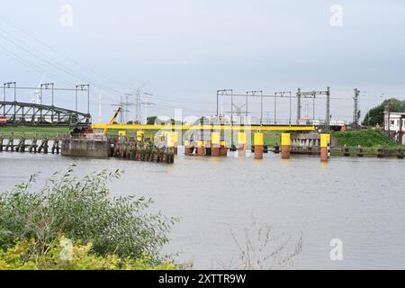 Elsfleth, Deutschland. August 2024. Die Arbeiter stellen sicher, dass die Brücke perfekt sitzt, damit die neue provisorische Brücke beim Anheben an ihrem Platz ist. Der „Athlet“-Schwimmkran bringt den 24 Meter langen und 58 Tonnen schweren Brückenabschnitt als Ersatz für die Eisenbahnbrücke, die einige Wochen zuvor von einem Tankfahrzeug gerammt wurde. Diese Brücke war auch eine provisorische Brücke, da bereits im Februar ein Lastkahn auf die reguläre Eisenbahnbrücke traf. Die Brücke und die Freileitungen wurden so stark beschädigt, dass der Zugverkehr eingestellt werden musste. Quelle: Lars Penning/dpa/Alamy Live News Stockfoto