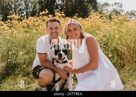 Lächelndes junges Paar mit Hund vor Wildblumen Stockfoto