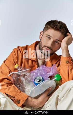 Ein Mann sitzt mit dem Kopf in der Hand, umgeben von Plastikmüll. Stockfoto