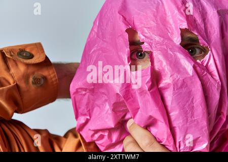 Ein Mann mit einer pinkfarbenen Plastiktüte über dem Gesicht, der durch ein Loch im Material schaut. Stockfoto