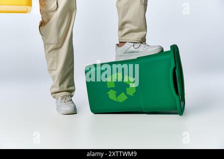 Der Fuß eines Mannes liegt auf einem grünen Recyclingbehälter, was die Bedeutung von Nachhaltigkeit unterstreicht. Stockfoto