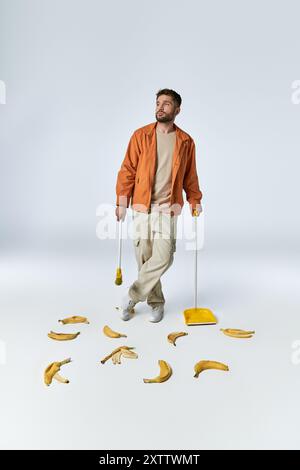 Ein Mann in einer orangefarbenen Jacke steht inmitten von Bananenschalen und hält einen Besen und eine Schüssel. Stockfoto