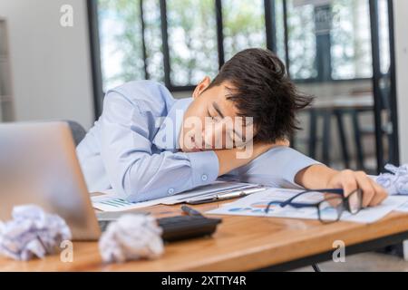 Müder und überarbeiteter junger Geschäftsmann, der während seiner späten Arbeit in seinem Büro in den Schlaf fällt Stockfoto