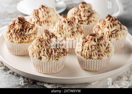 Delikate Tiramisu Cupcakes mit cremiger Mascarponcreme und Kakao serviert mit Kaffee in Nahaufnahme auf einem Teller auf einem Tisch. Horizontal Stockfoto